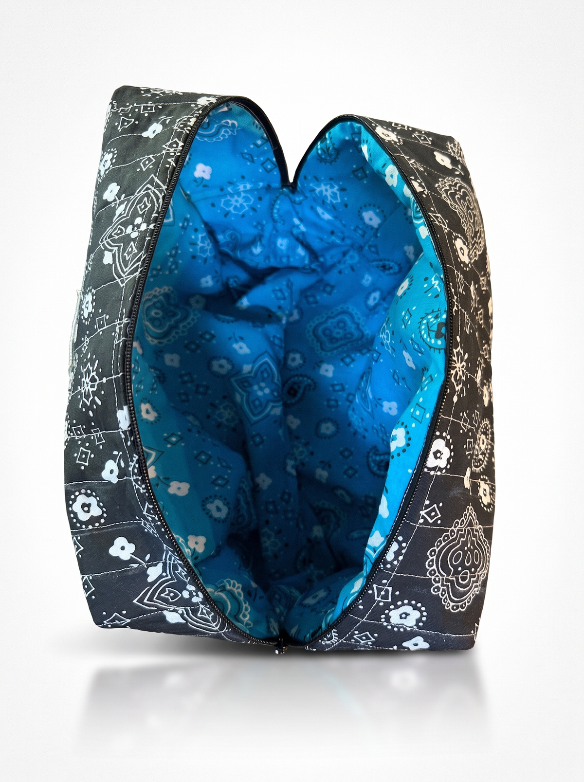 An open zippered pouch or cosmetic bag with a black and white paisley bandana print exterior and a bright blue patterned lining, shown on a white background.