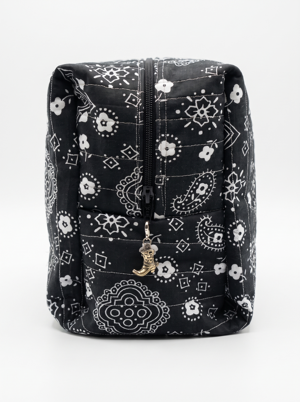 A black and white bandana-patterned quilted pouch with a front zipper and a small gold cowboy boot charm, shown against a plain white background.