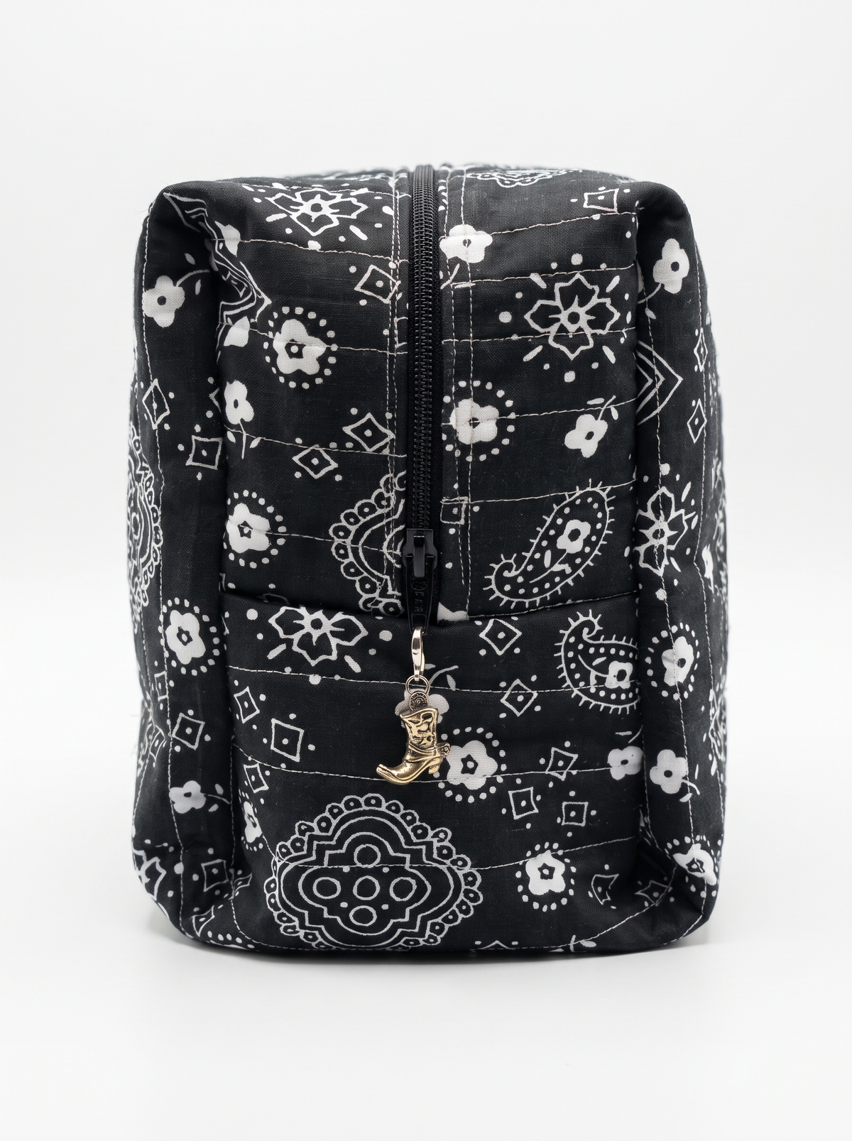 A black and white bandana-patterned quilted pouch with a front zipper and a small gold cowboy boot charm, shown against a plain white background.