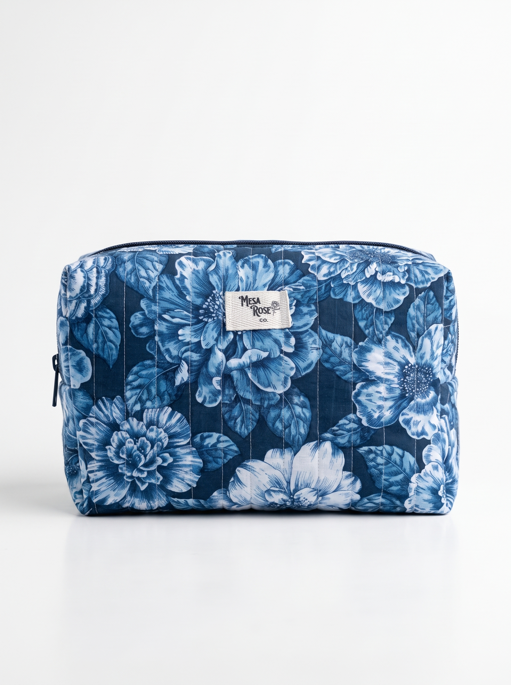 A rectangular zippered cosmetic pouch by Mesa Rose Co featuring a blue and white floral print, set against a plain white background.