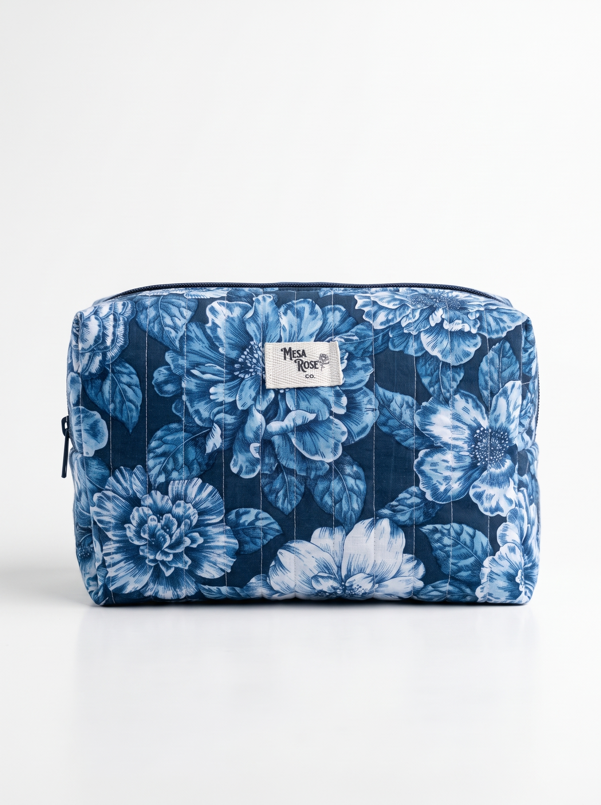 A rectangular zippered cosmetic pouch by Mesa Rose Co featuring a blue and white floral print, set against a plain white background.
