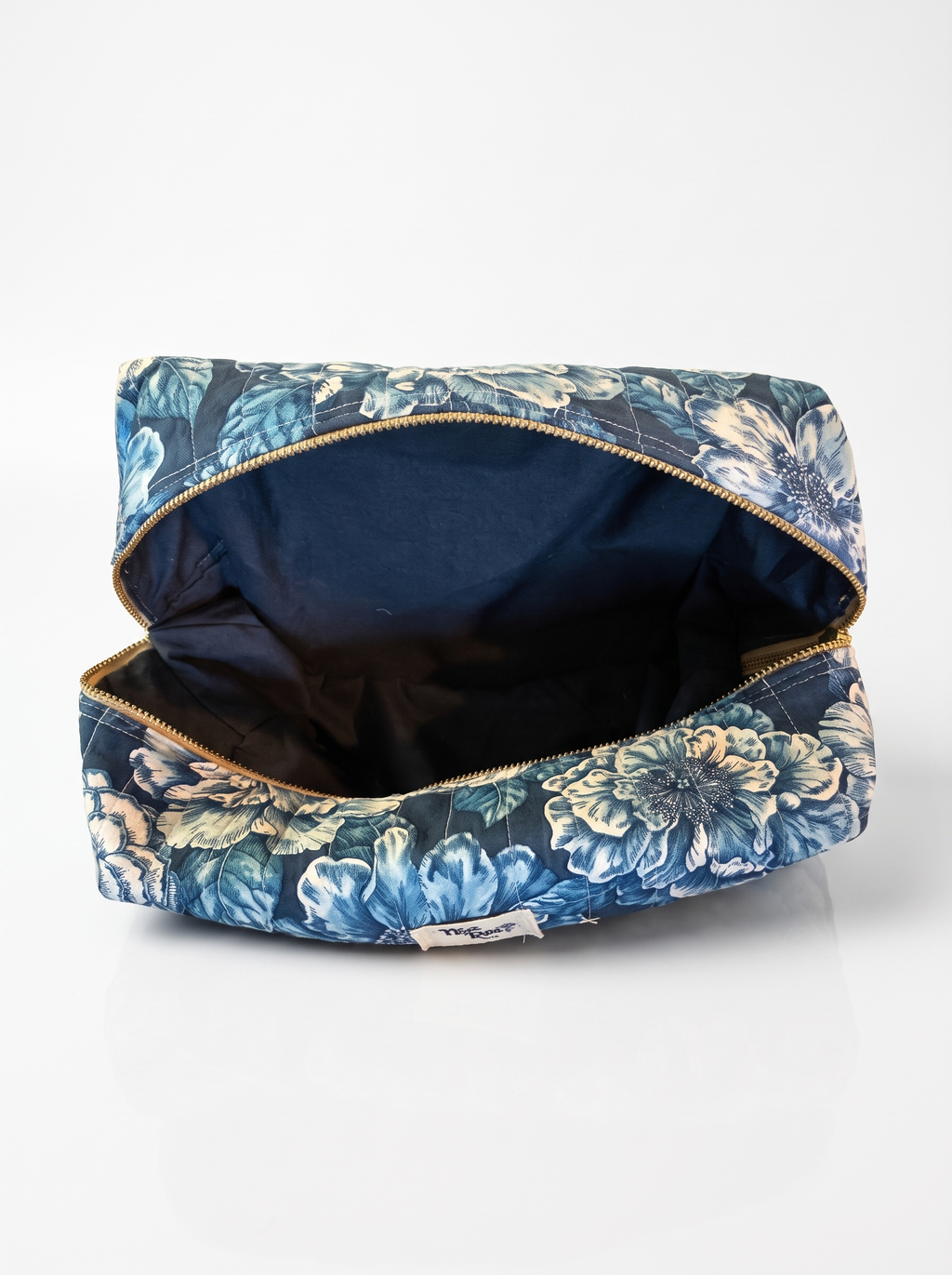 An open cosmetic pouch with a blue and white floral print exterior, a dark navy interior, and gold-tone zippers, shown on a clean white background.