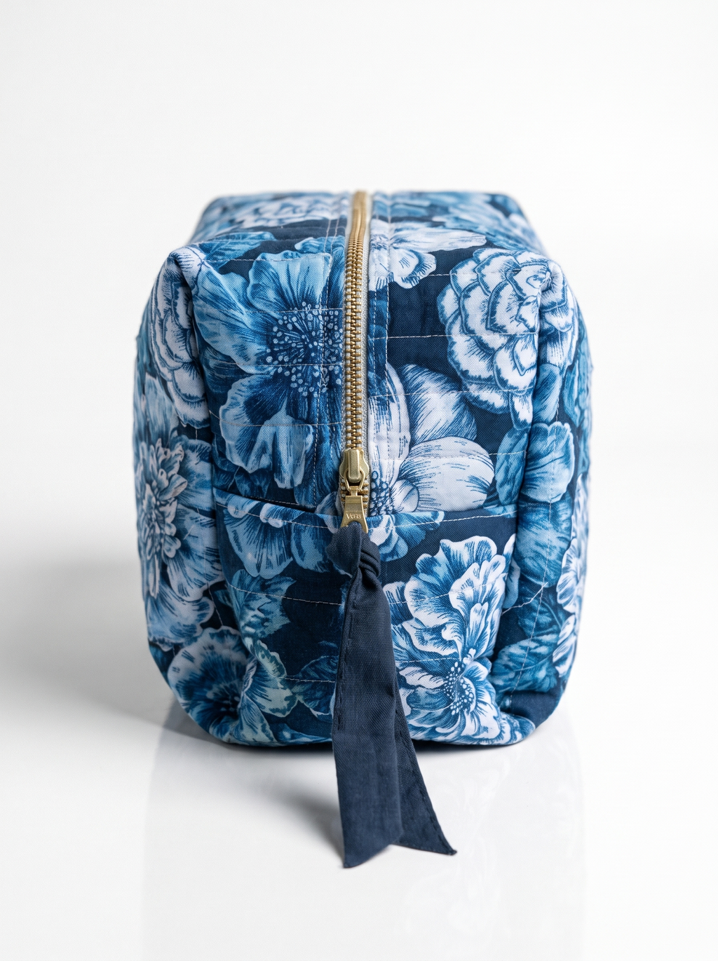 A blue and navy floral toiletry bag with a gold zipper and a dark blue fabric tassel pull, shown on a clean white background.