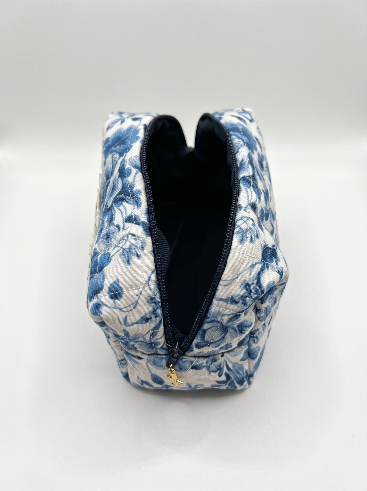 A blue and white floral toiletry bag with a black zipper and a small gold pull, shown open on a light gray background.