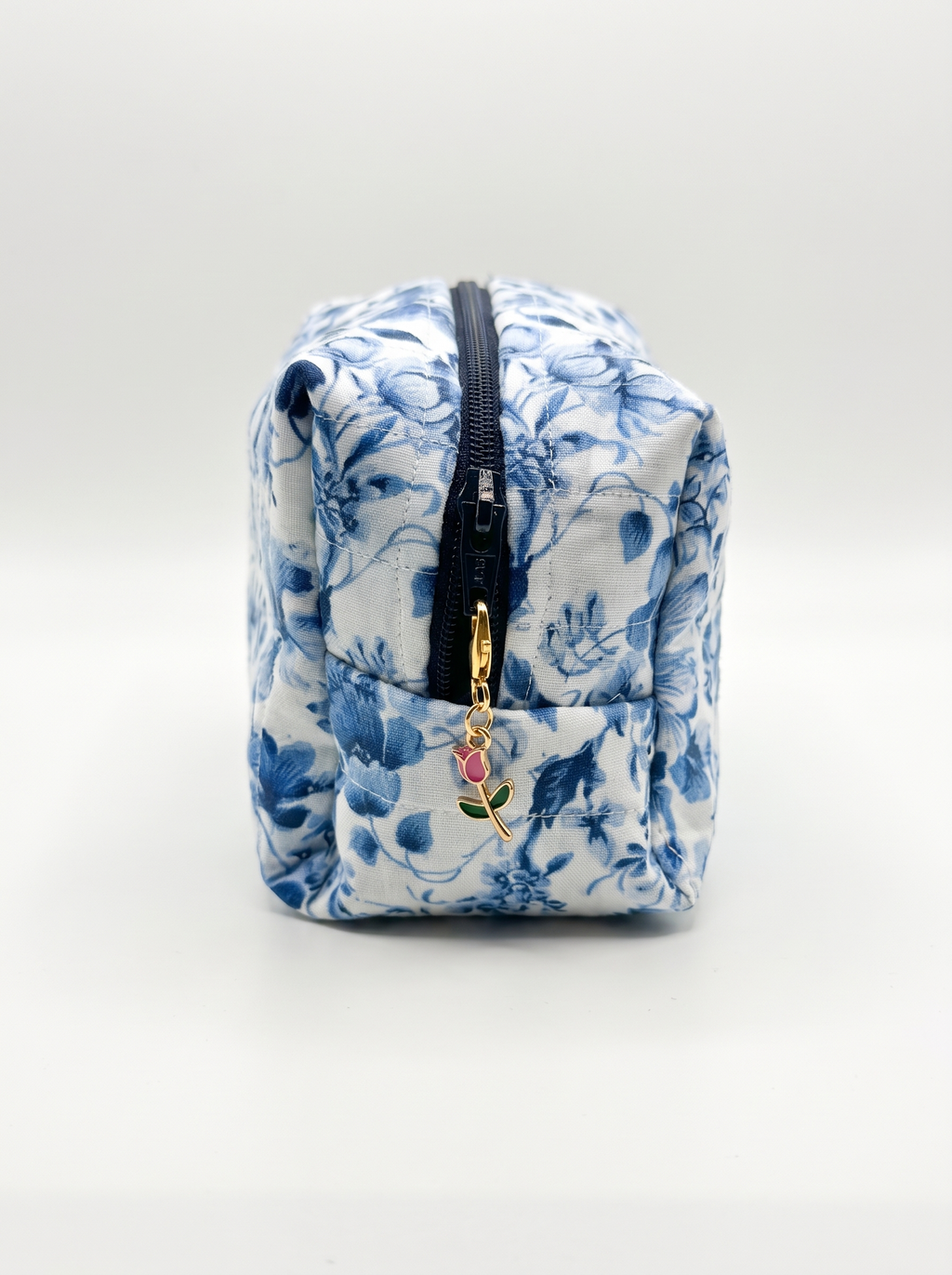 A small zippered pouch with a blue and white floral pattern, featuring a black zipper and a small gold charm with a pink rose.