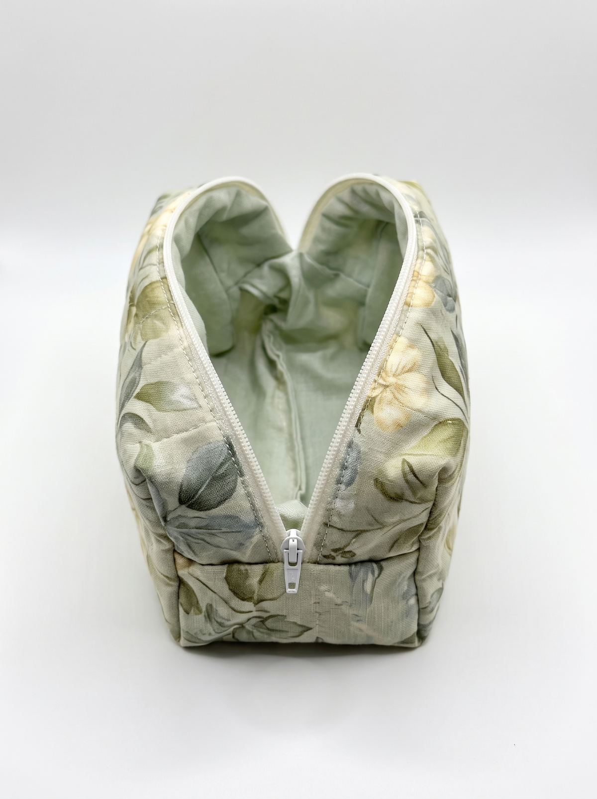 A zippered cosmetic pouch with a sage green and beige floral pattern, shown open against a light gray background.