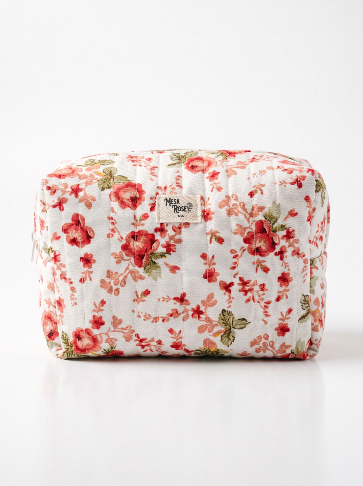 A quilted cosmetic pouch with a red and pink floral print on a white background, featuring a small 'Mesa Rose' brand label on the front.